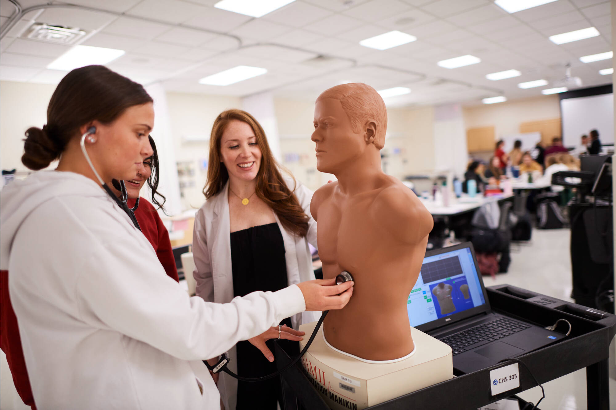 Lauren Vachon observing students using a stethescope on a mannequin